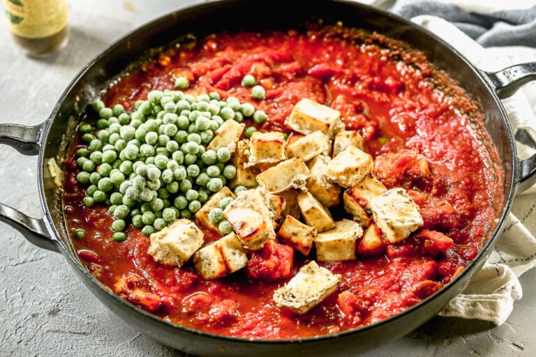 adding baked paneer cheese and frozen peas to a skillet of paneer tikka masala with tomato sauce