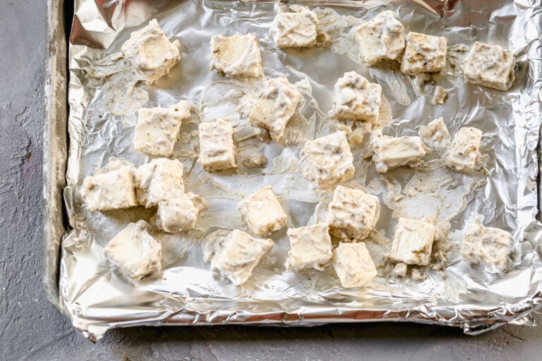 cubes of marinated paneer cheese on a foil-lined sheet pan ready to bake