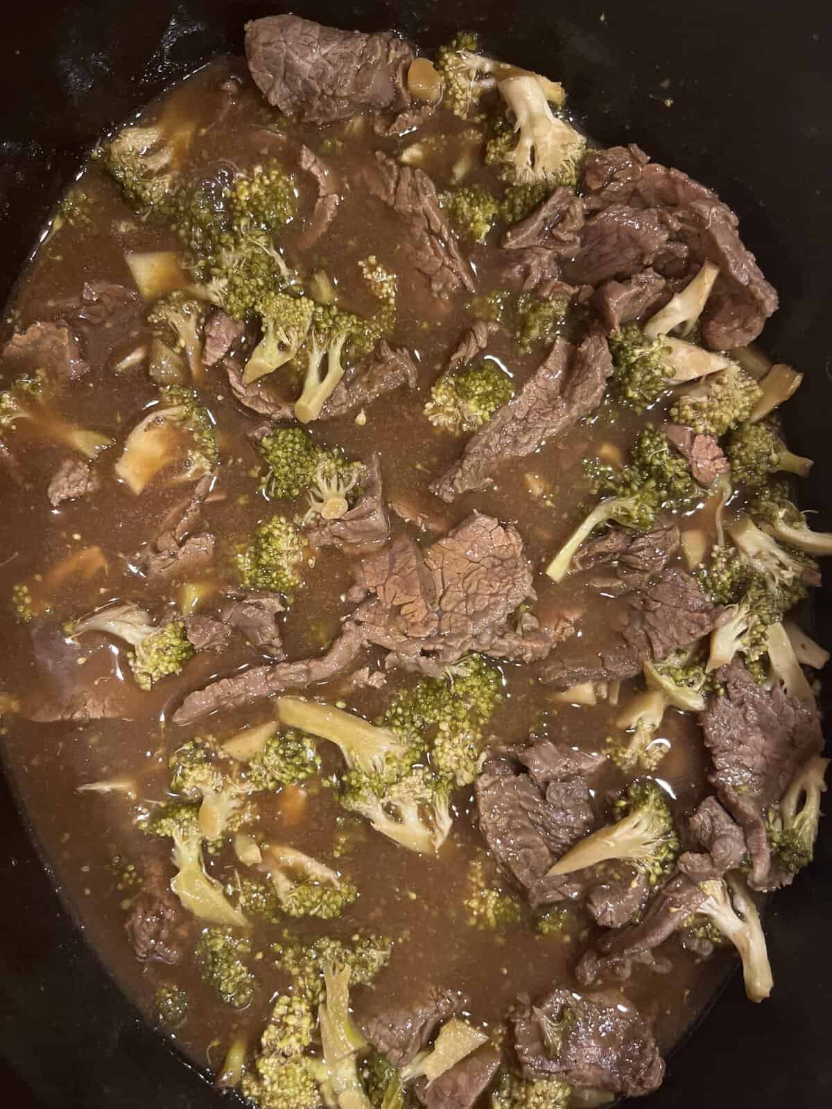 Beef and broccoli in a rich brown sauce, cooked together in a black pot or slow cooker.