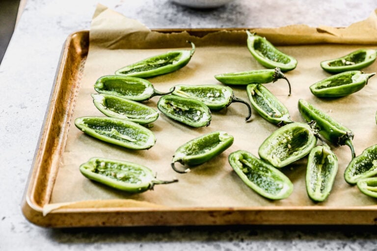 jalapeno peppers cut in half on a sheet pan with seeds removed