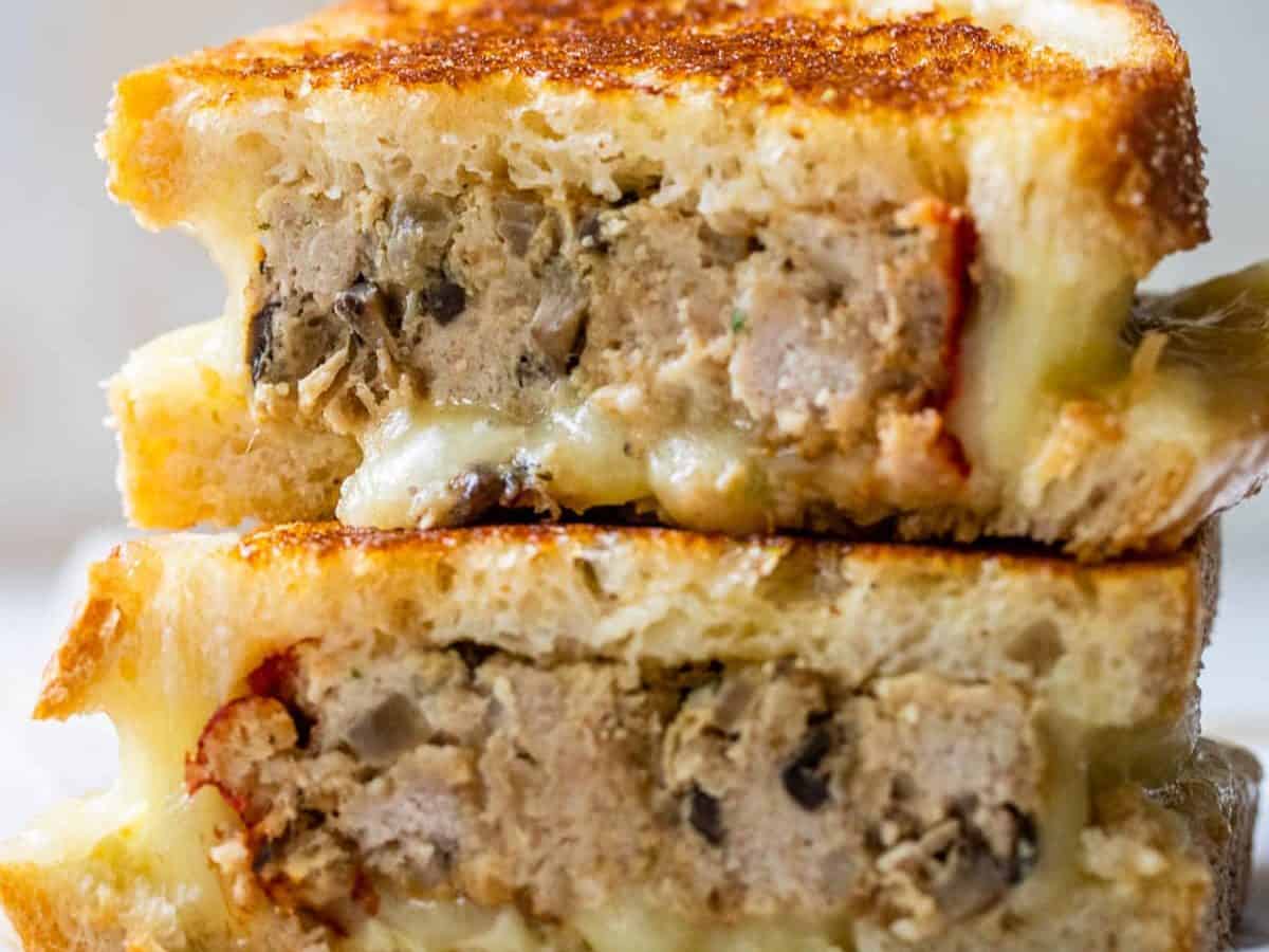 A grilled cheese sandwich filled with slices of meatloaf, stacked in two halves on a wooden surface.