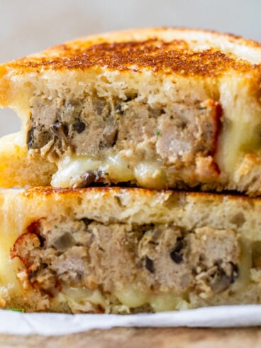 A grilled cheese sandwich filled with slices of meatloaf, stacked in two halves on a wooden surface.