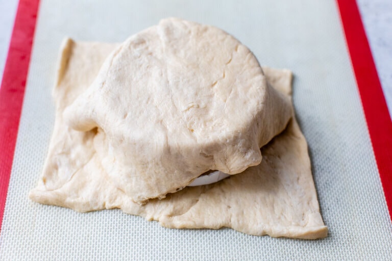 Dough being wrapped around a round piece of cheese