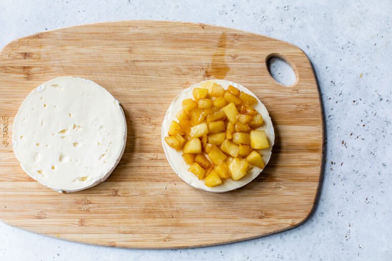Apples sitting on a slice of brie on a wooden cutting board
