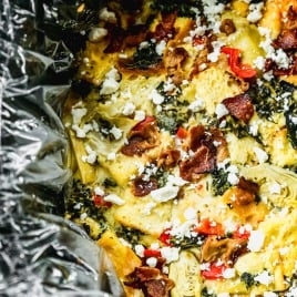 Breakfast casserole with bacon, artichokes, spinach, and feta cheese in a foil-lined dish.