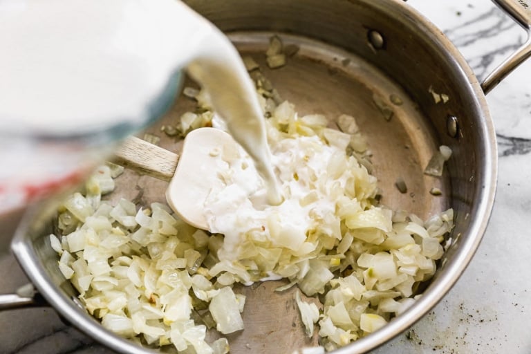 adding milk to a pan of sauteed onions for cheesy scalloped potatoes