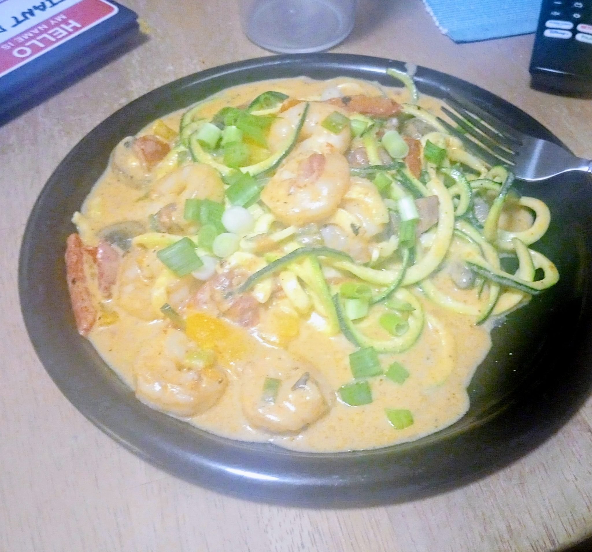 A plate of shrimp in a creamy sauce with spiralized zucchini, bell peppers, and green onions, with a fork on the side.