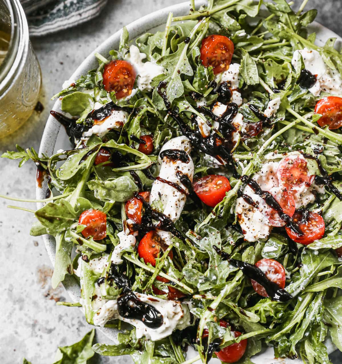 salad with burrata cheese, tomato, arugula, and balsamic glaze in a large bowl