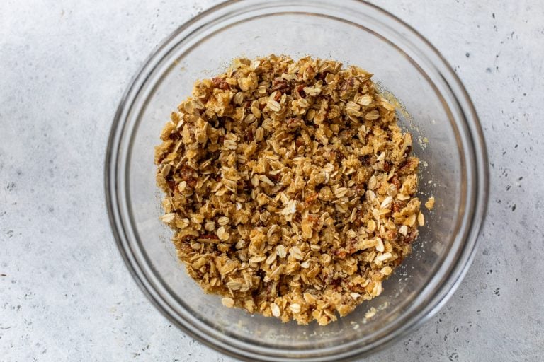 A glass bowl filled with oat and nut crumble topping on a light gray surface.
