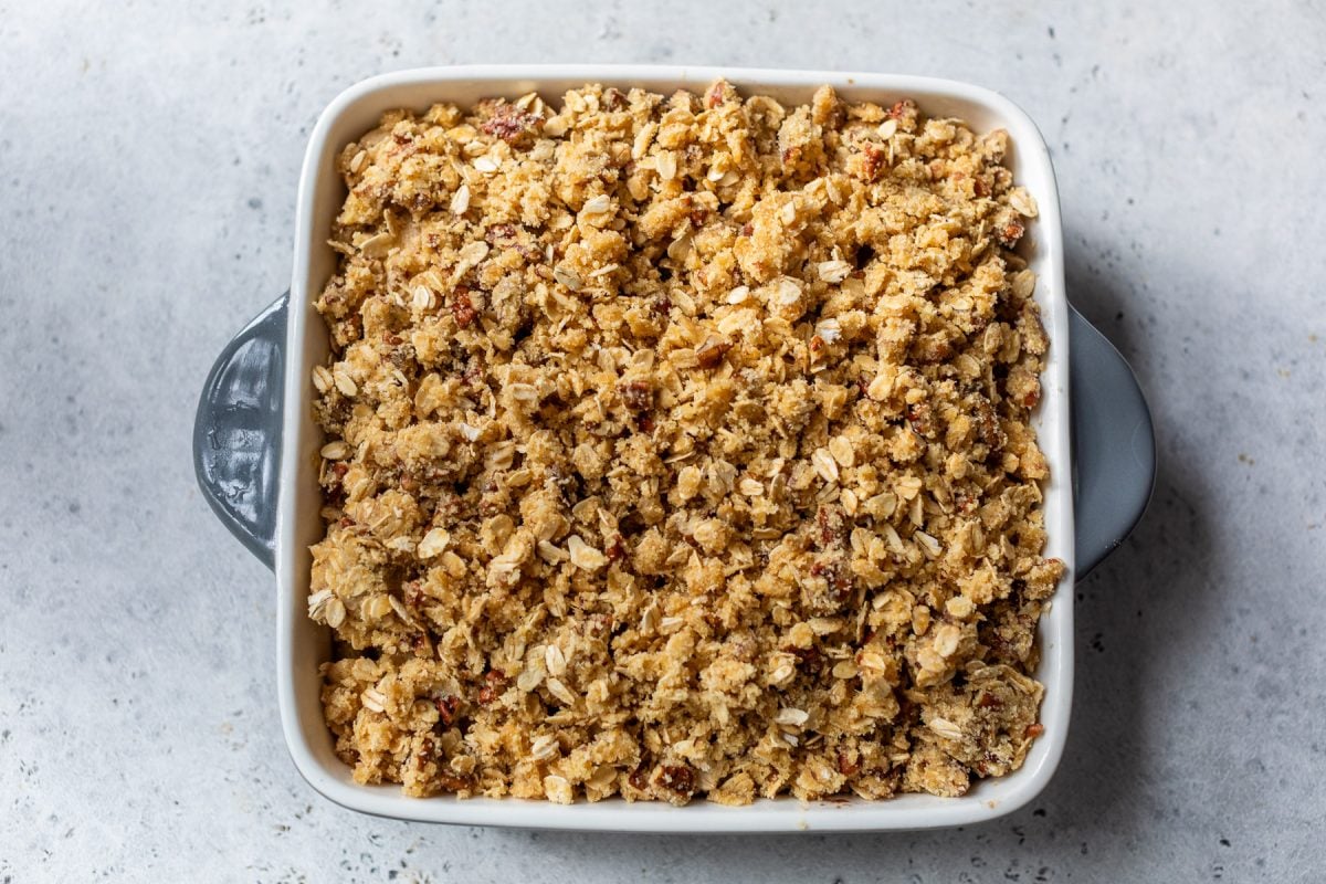 A square baking dish filled with unbaked gluten free apple crisp on a light gray surface.