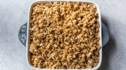 A square baking dish filled with unbaked gluten free apple crisp on a light gray surface.