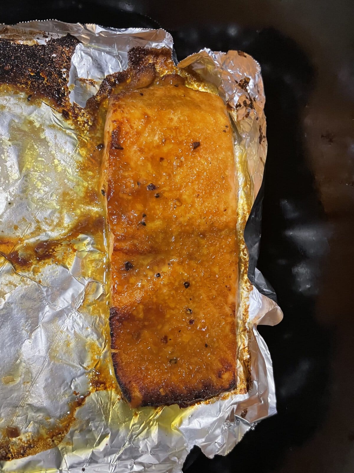 Seasoned, baked salmon fillet on foil with a golden-brown crust, resting on a dark surface.