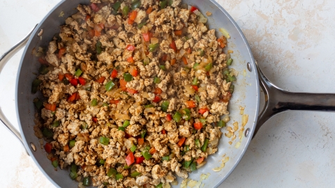 A skillet filled with cooked ground meat, diced red and green bell peppers, and onions, all mixed together and lightly browned.