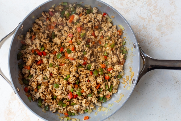 A skillet filled with cooked ground meat, diced red and green bell peppers, and onions, all mixed together and lightly browned.