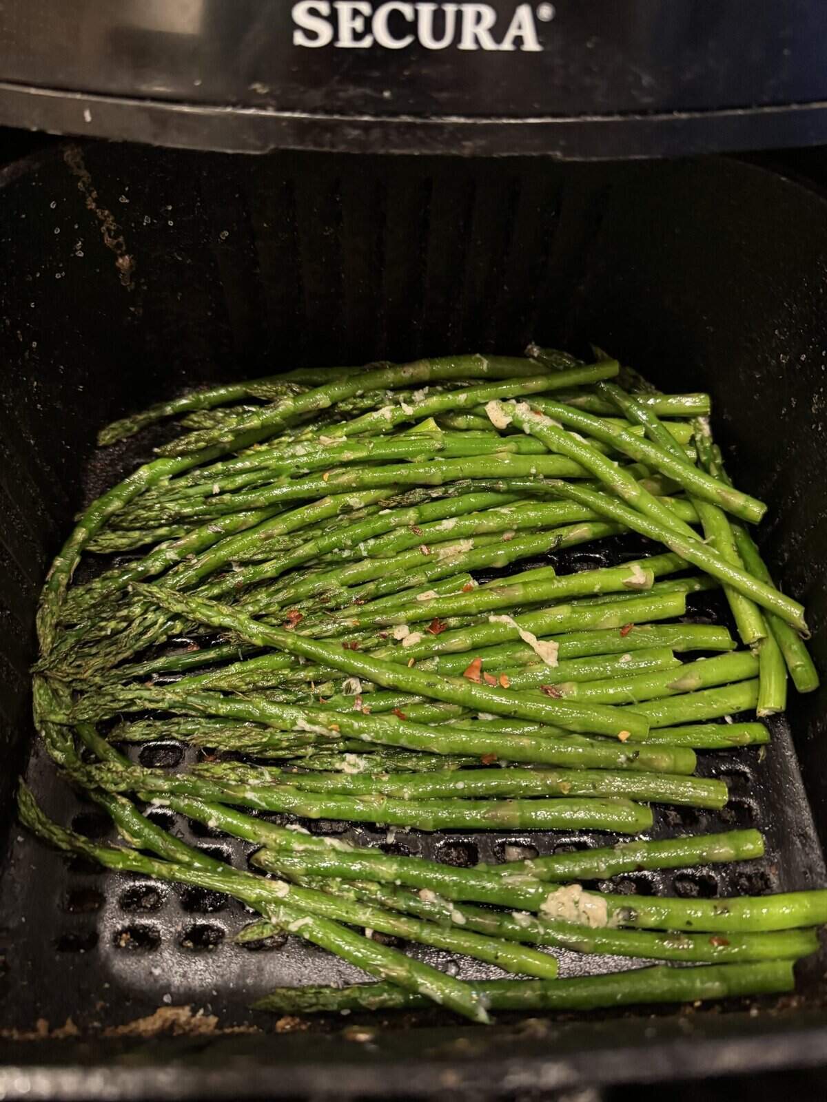 Fresh asparagus spears with seasoning in an air fryer basket, ready to be cooked.