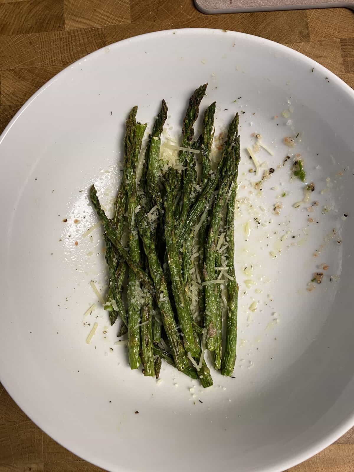 Roasted asparagus spears topped with grated cheese and seasoning on a white plate, partially eaten.