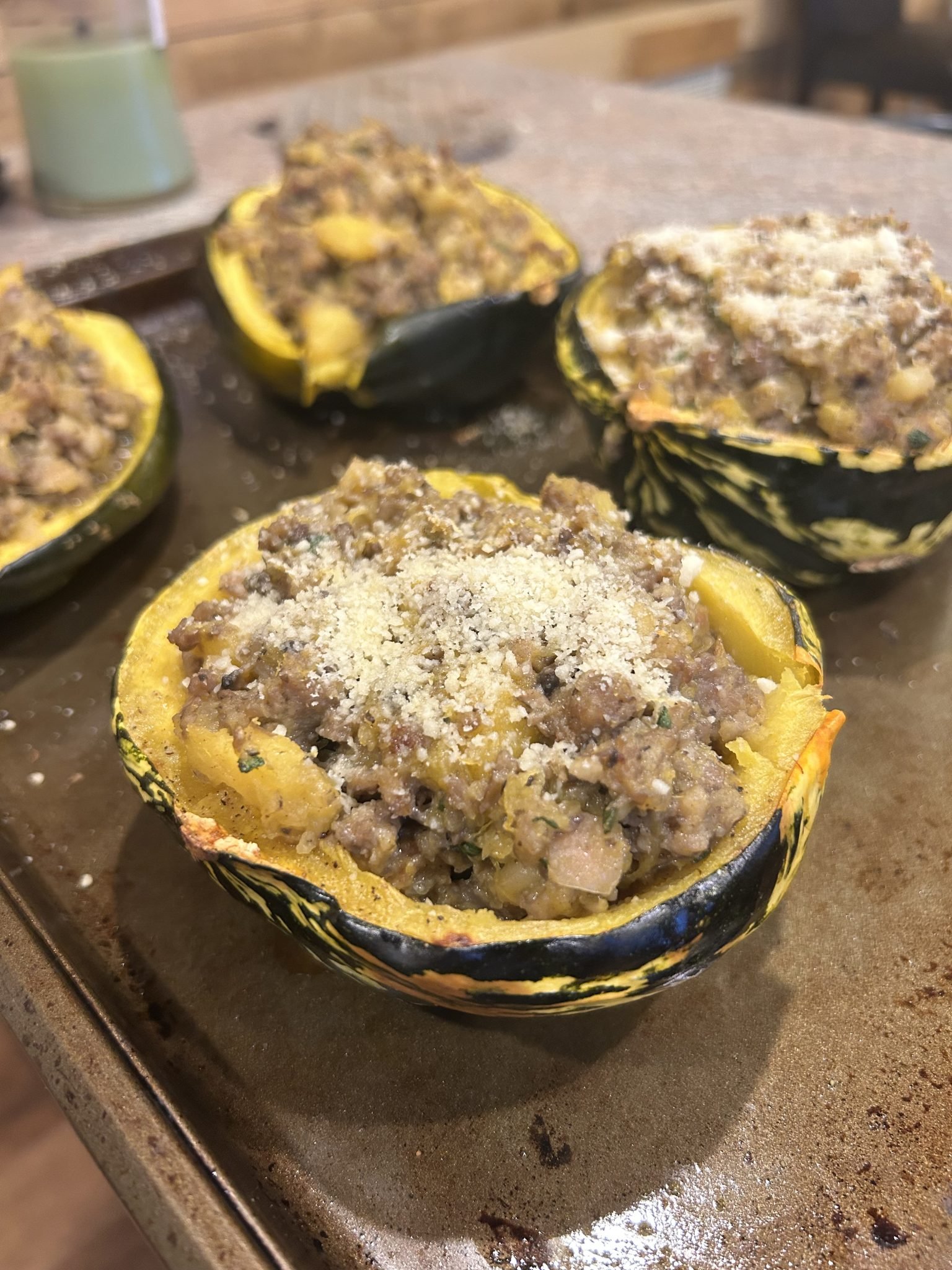 Halved squash filled with a seasoned meat mixture, topped with grated cheese, on a baking sheet.