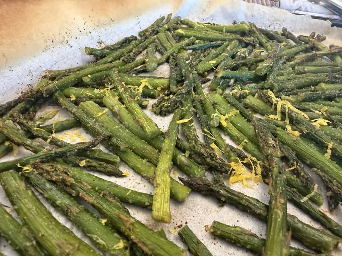 Roasted asparagus spears on parchment paper, garnished with lemon zest.