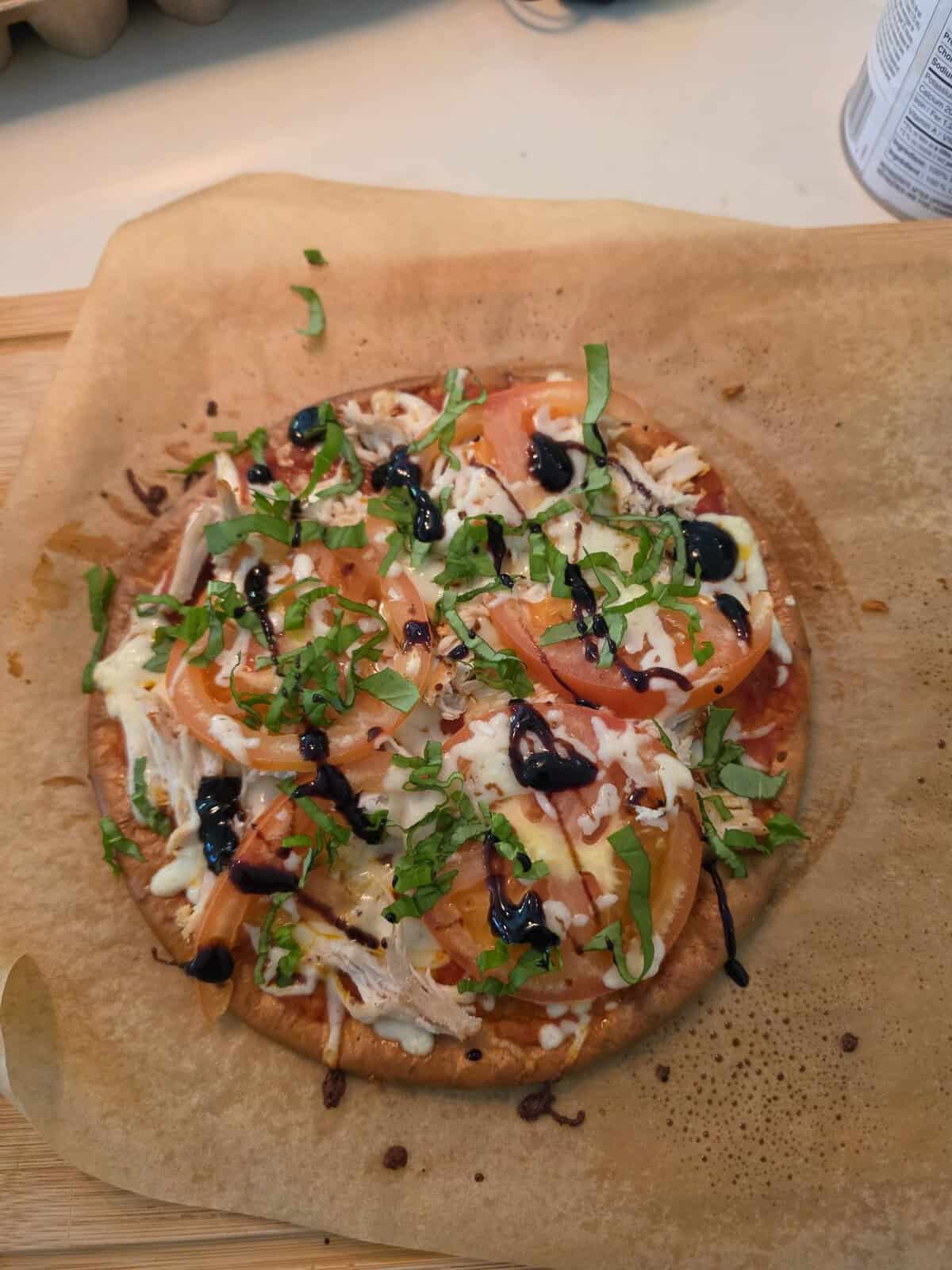 Individual pizza topped with sliced tomatoes, chicken, fresh basil, and a balsamic glaze drizzle.