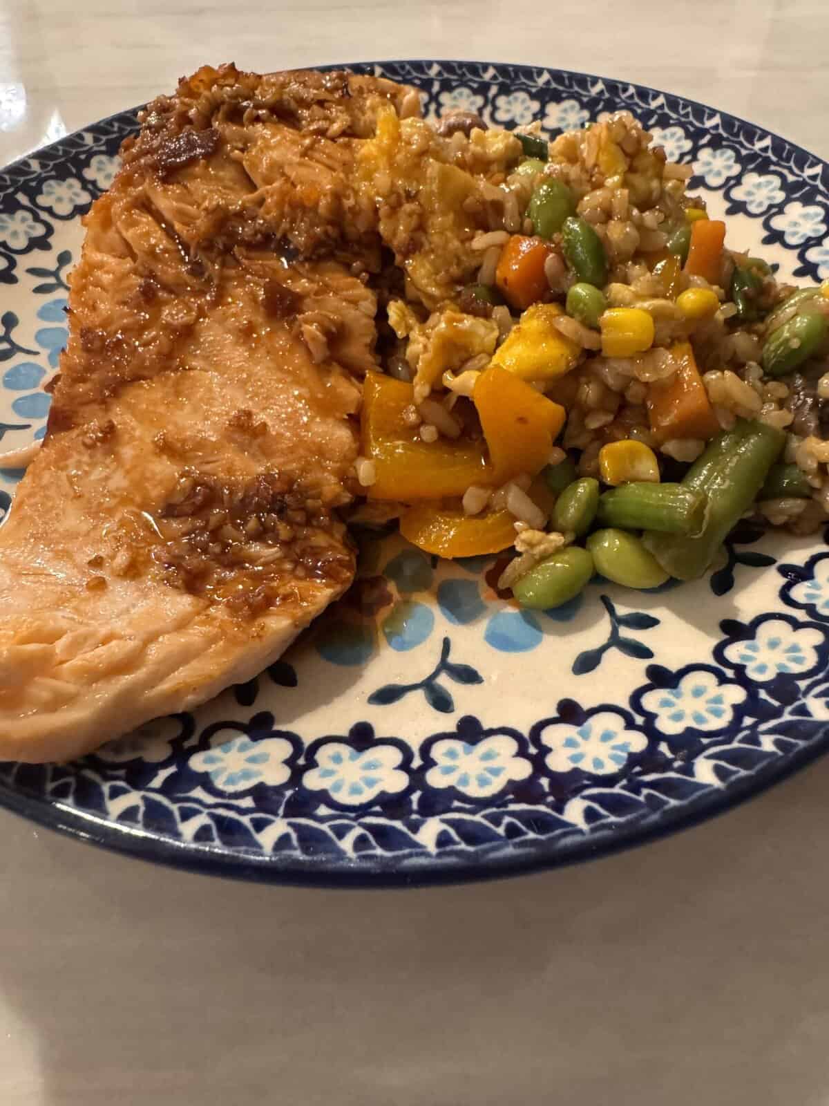 A plate with a cooked salmon fillet and a serving of rice with mixed vegetables.