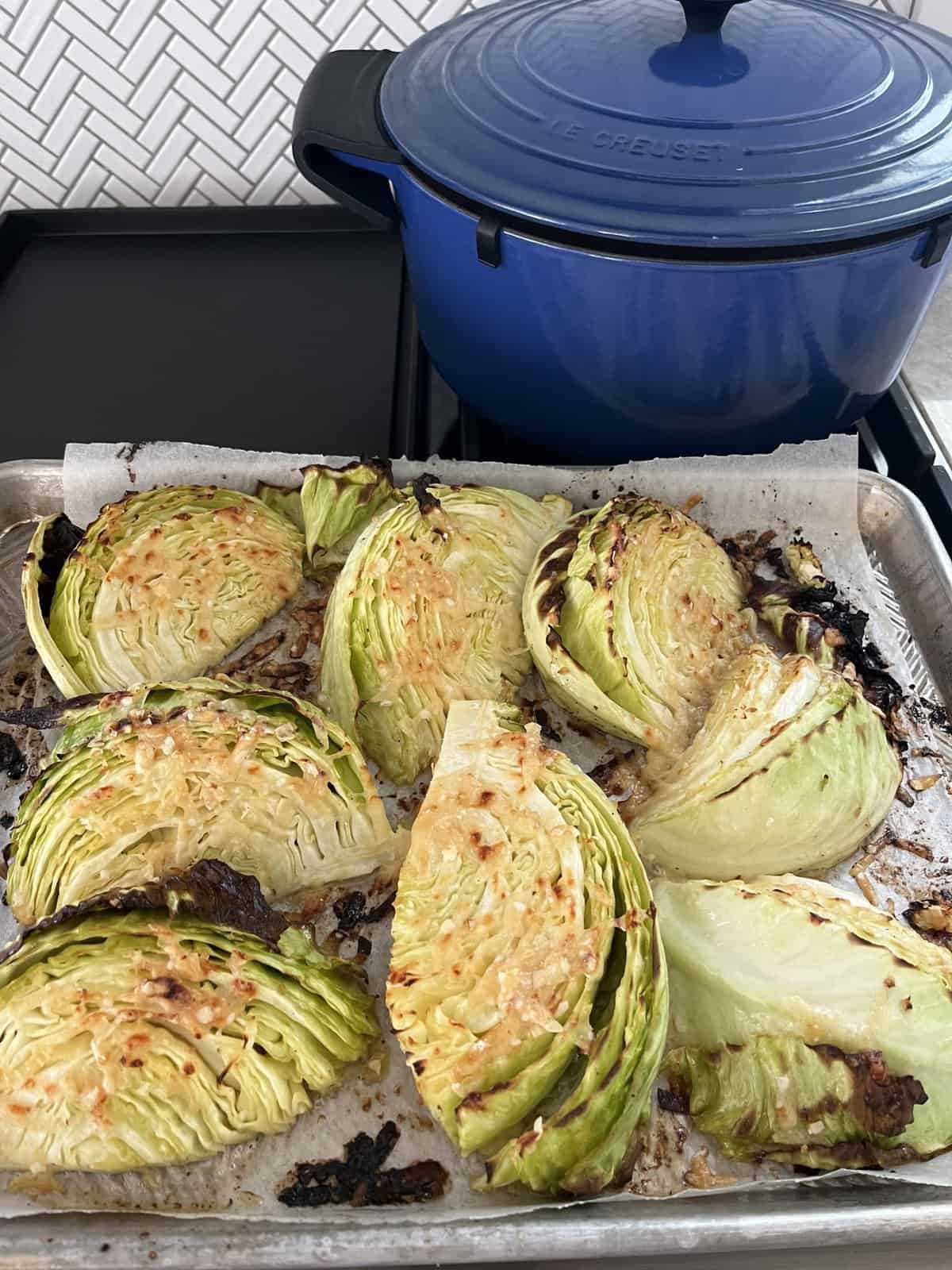 Roasted cabbage wedges on a baking tray with a blue Dutch oven in the background on the stove.