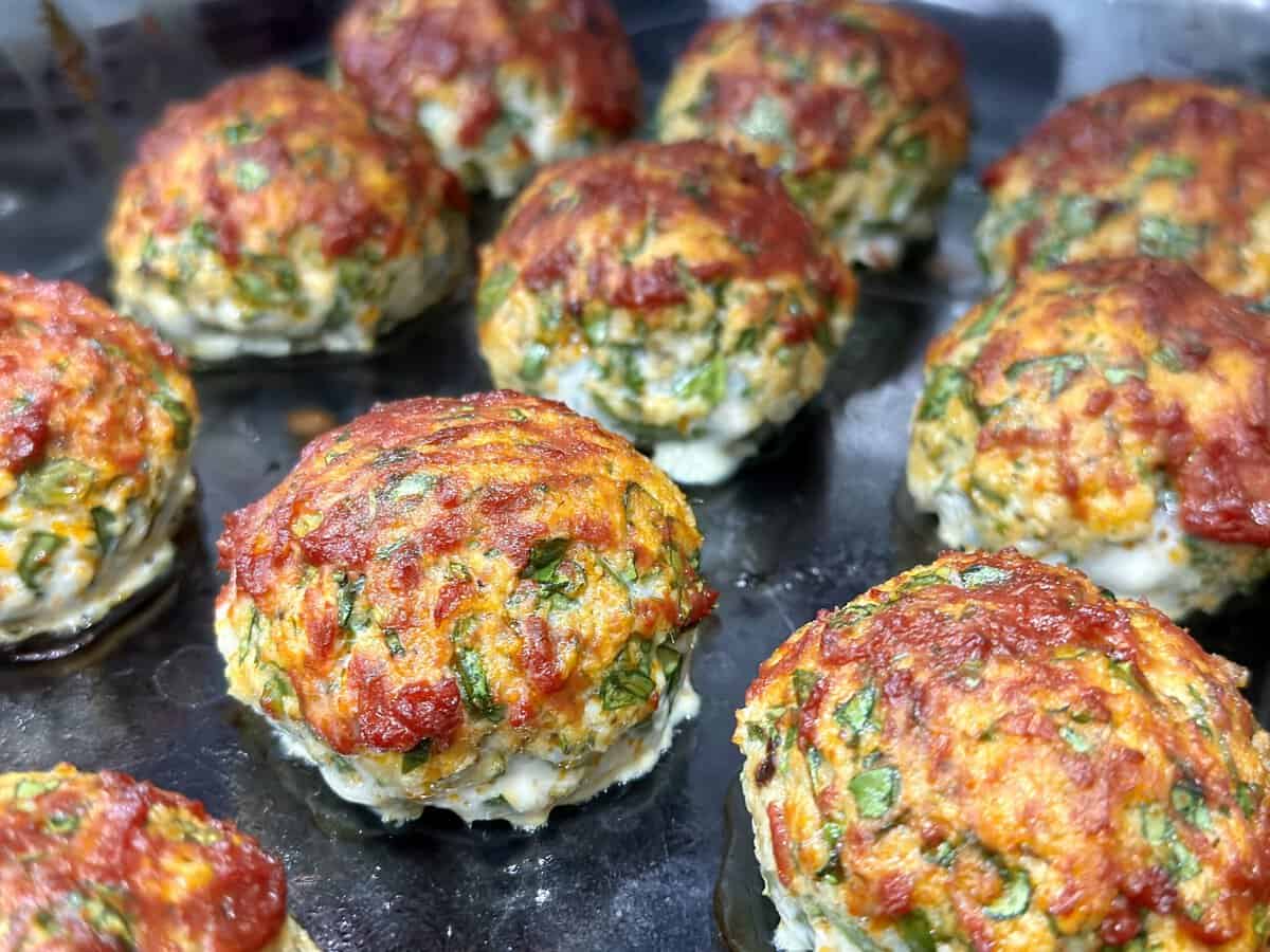 Baked meatballs with herbs and tomato sauce on a dark baking tray, golden brown and freshly cooked.