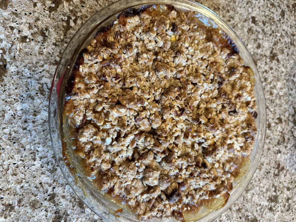 A freshly baked fruit crisp with a golden-brown oat topping in a round glass dish on a speckled countertop.