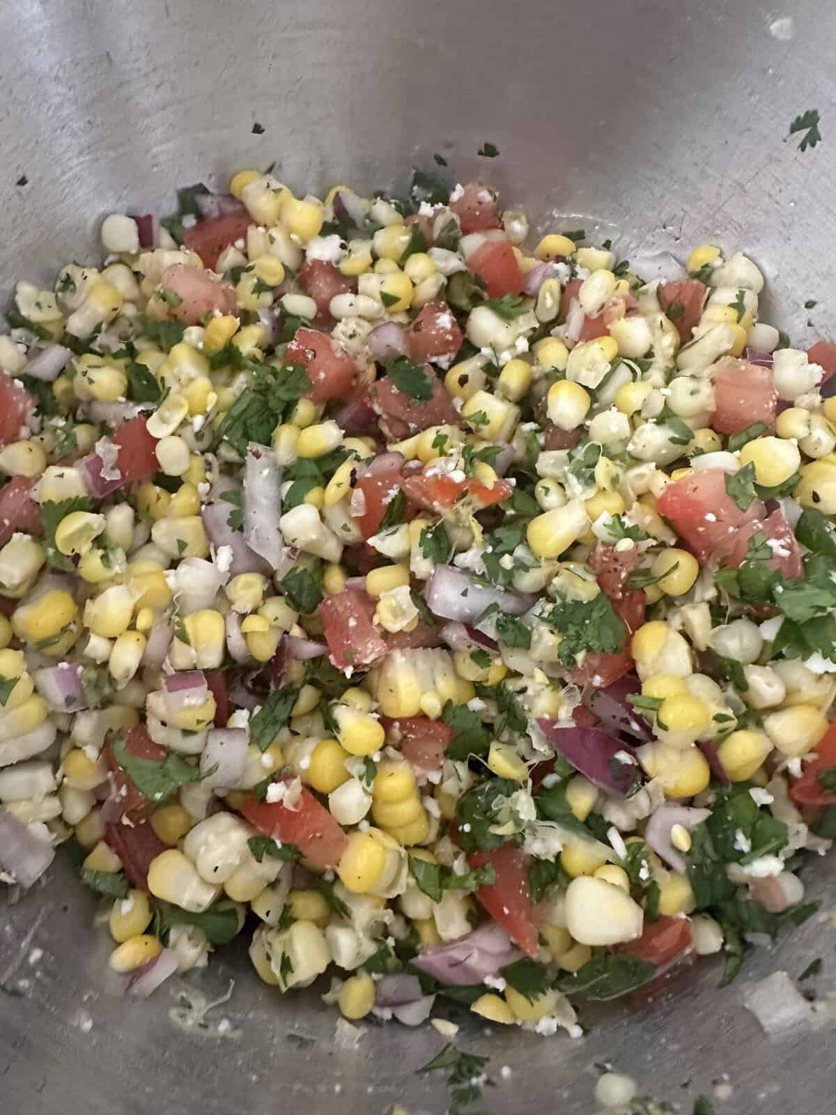 Chopped corn, tomato, red onion, cilantro, and green pepper mixed in a metal bowl.
