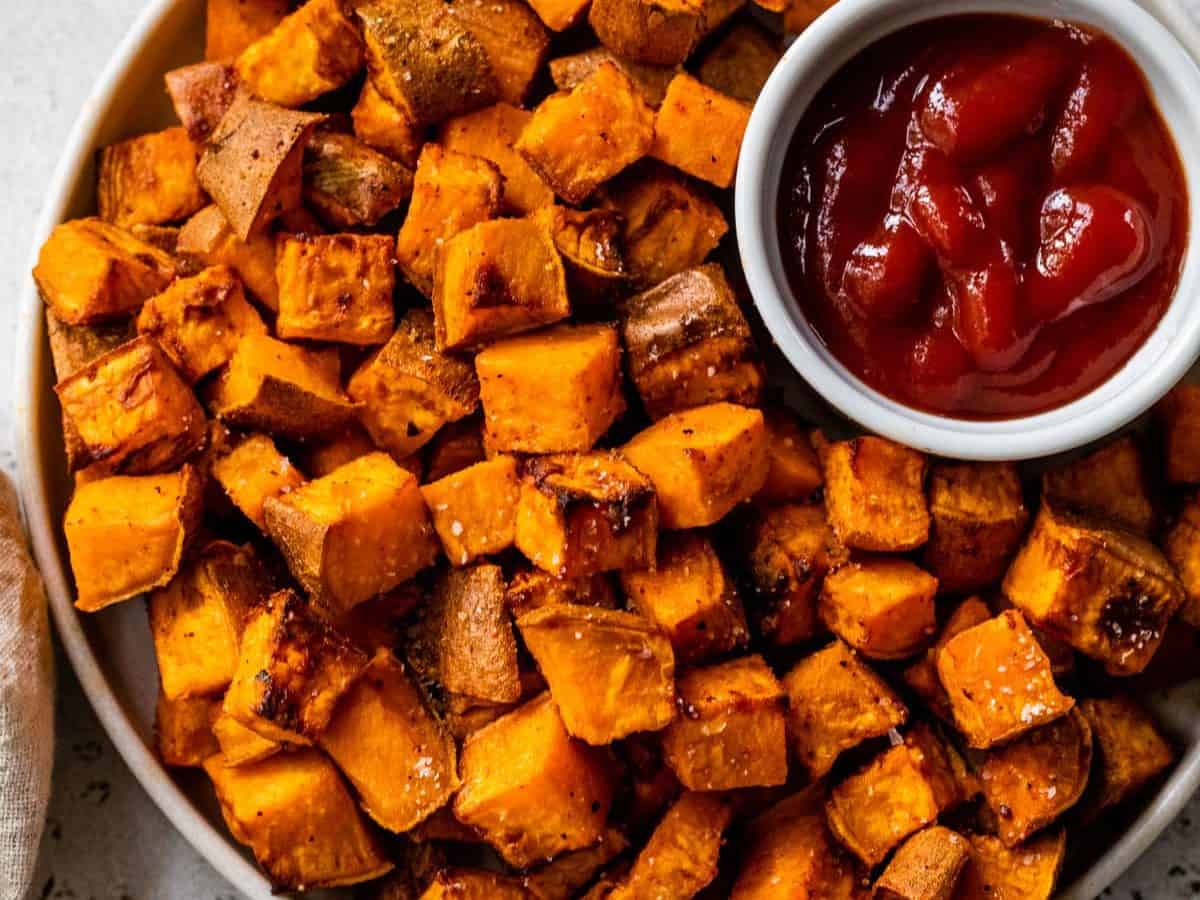 Overhead view of air fryer sweet potato cubes in bowl with bowl of ketchup