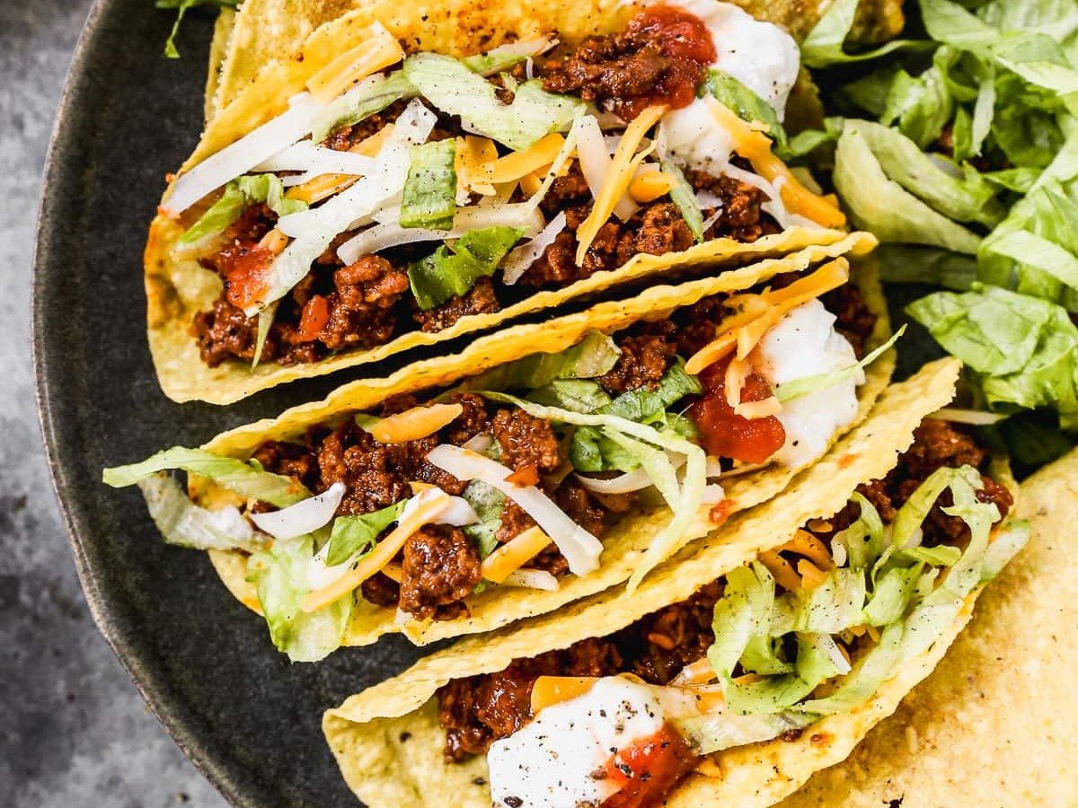 Hard shell ground beef tacos on plate with toppings