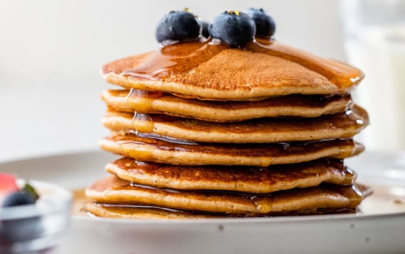 Stack of protein pancakes on plate with syrup and blueberries