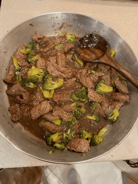 Beef and broccoli stir fry in a pan with a wooden spoon, on a kitchen counter.