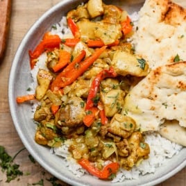 A bowl of rice topped with coconut curry chicken, red bell peppers, and naan bread on the side.