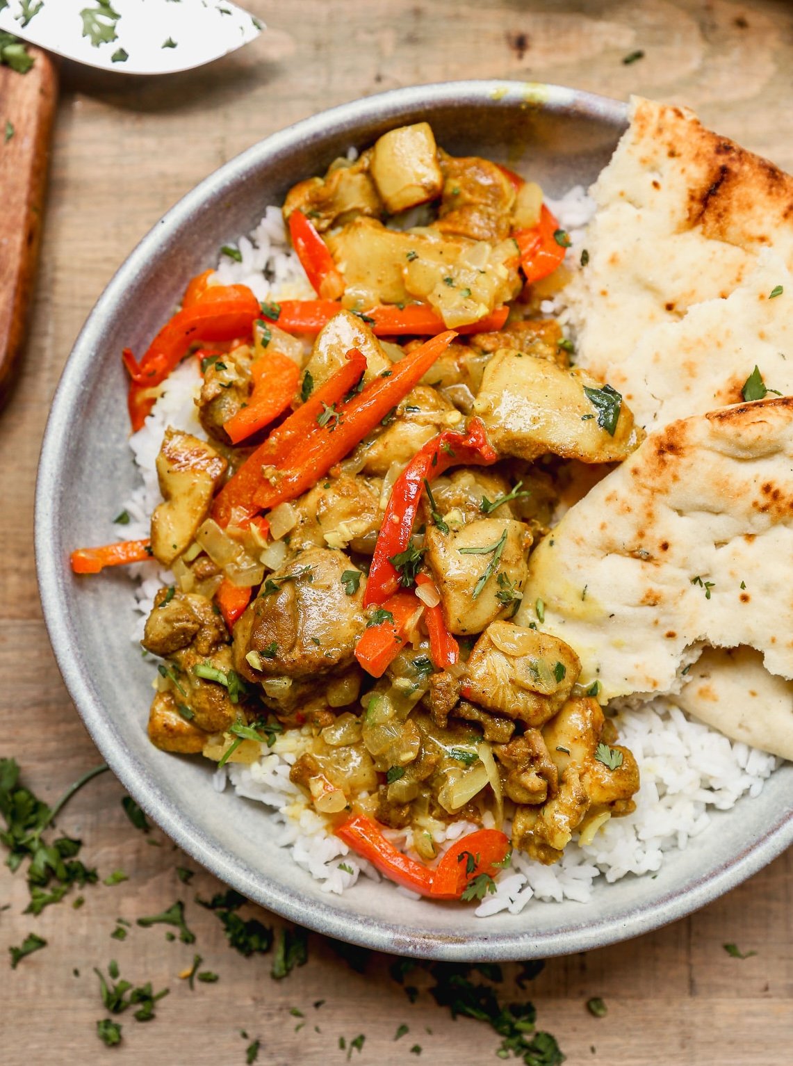 A bowl of rice topped with coconut curry chicken, red bell peppers, and naan bread on the side.