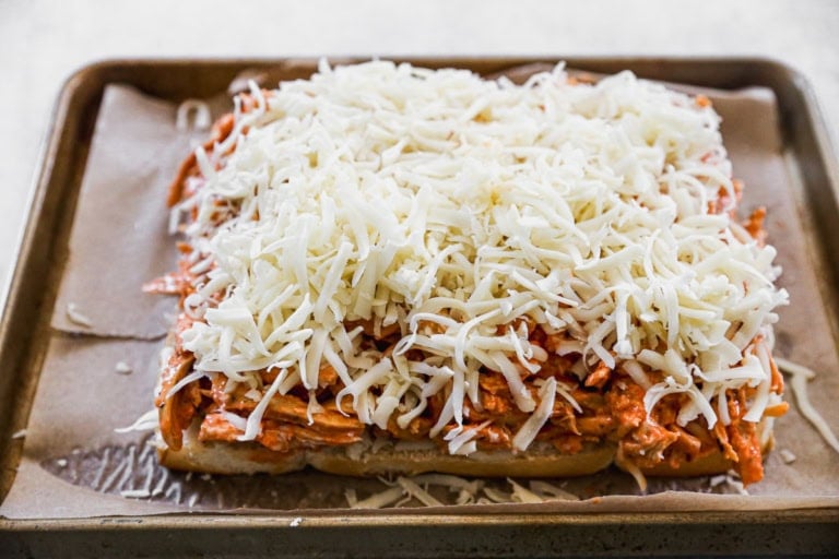 An open-faced sandwich on a baking sheet topped with shredded chicken in sauce and lots of shredded cheese.