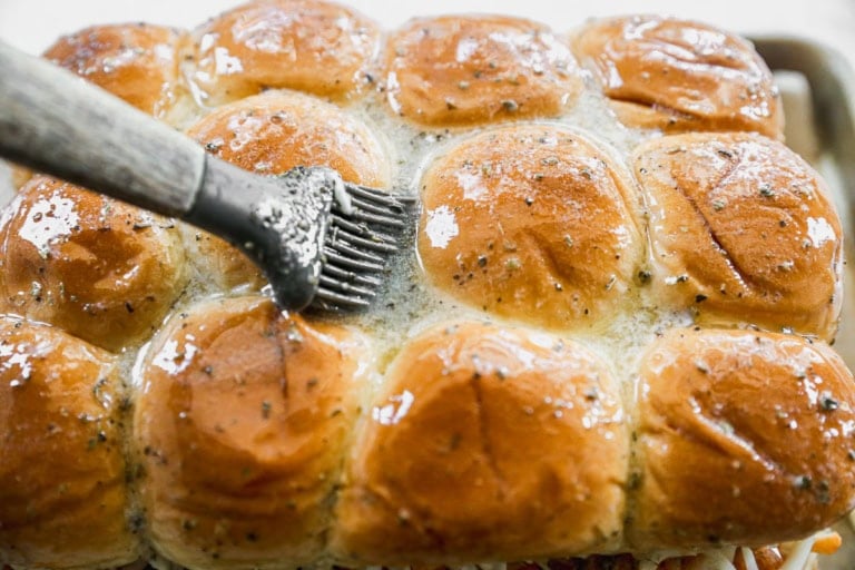 Brushing herbed butter onto Hawaiian rolls for sliders
