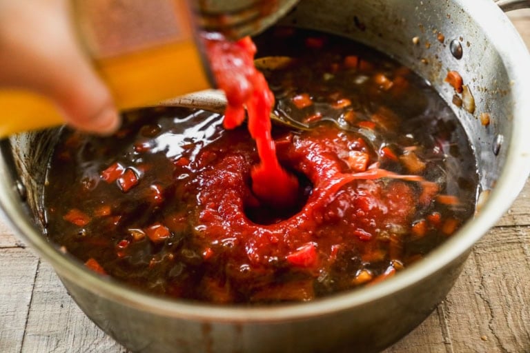Pouring tomatoes into pot of cowboy stew
