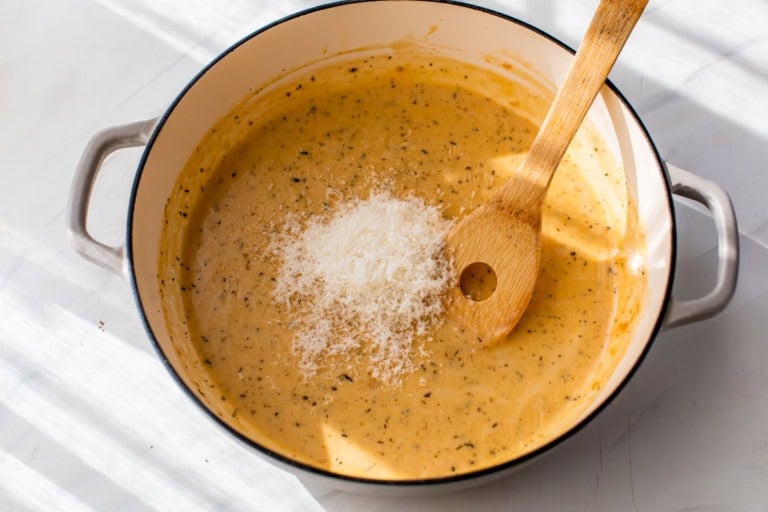 Stirring grated parmesan into creamy sauce