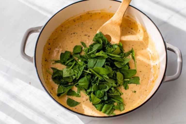 Stirring chopped spinach into creamy sauce