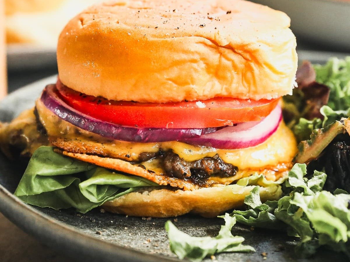 a double stacked smash burger on a bun with cheese, lettuce, and tomato