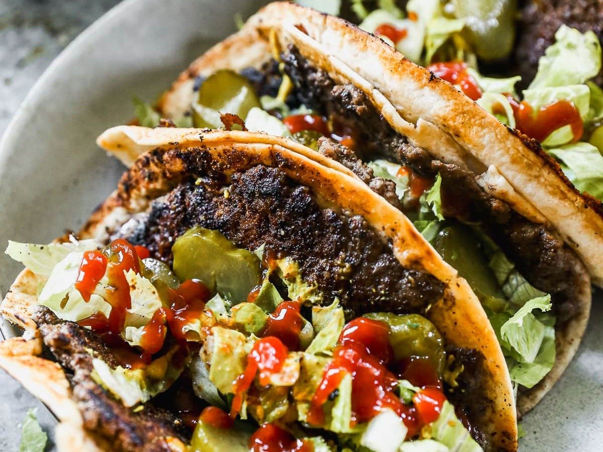 Smash tacos on plate with lettuce, ketchup, and mustard