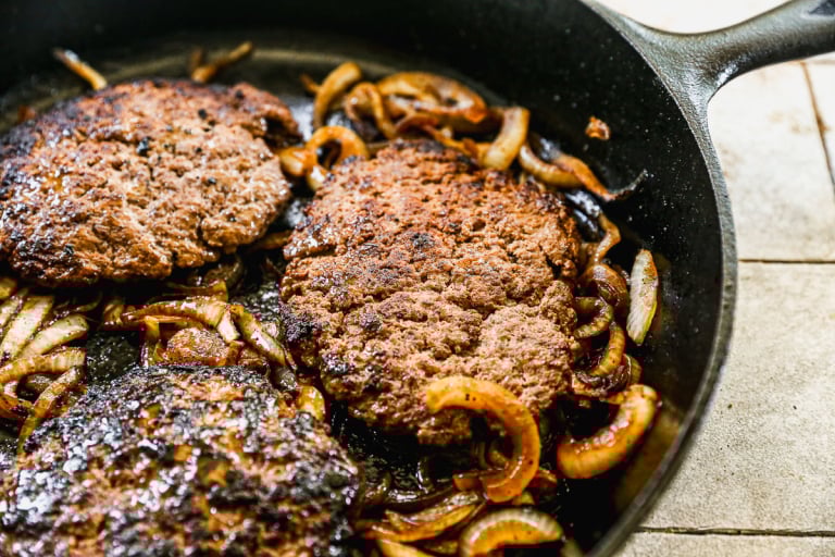 Patties cooking in skillet with onions