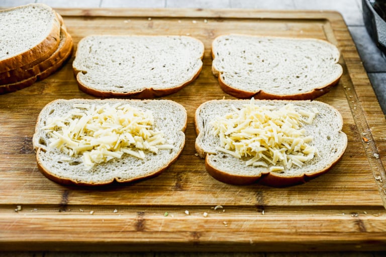 4 slices of bread on cutting board, with 2 topped with cheese