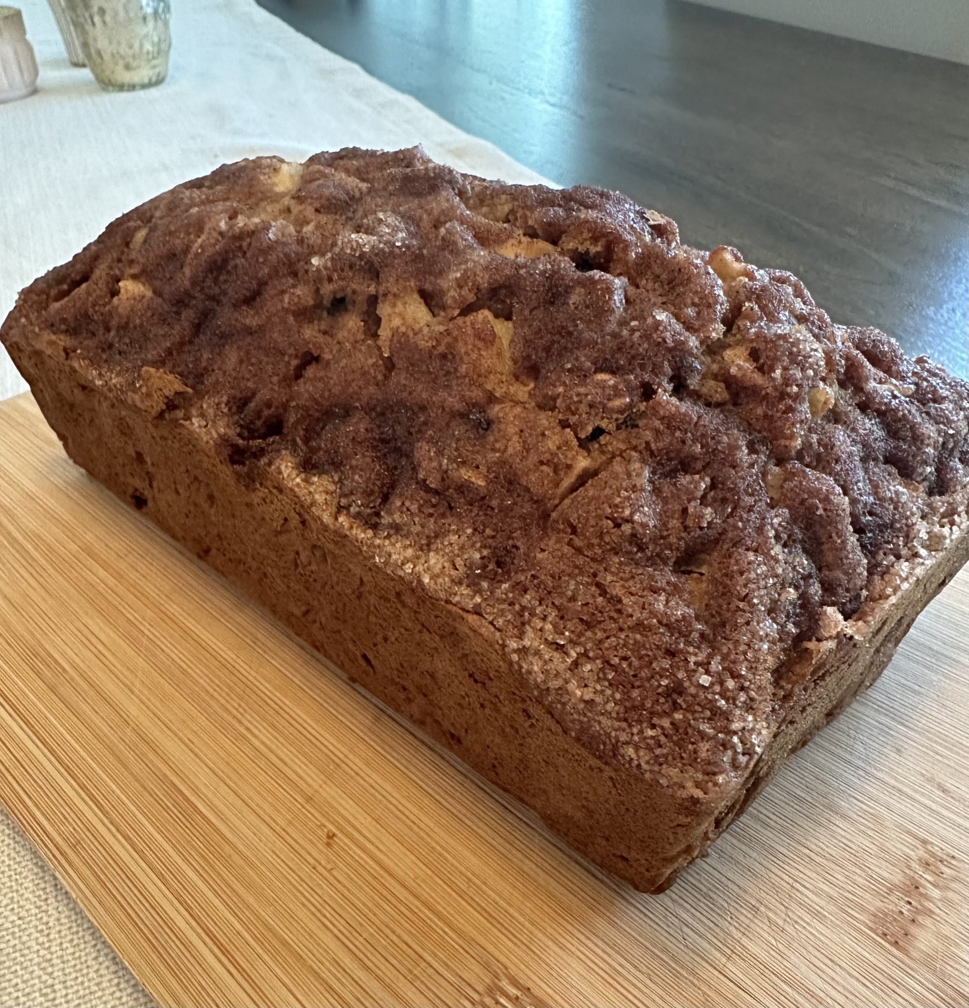 A loaf of cinnamon sugar bread sits on a wooden cutting board on a table.
