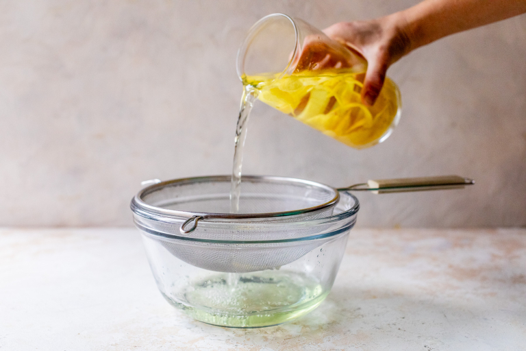 Pouring infused vodka through strainer into bowl