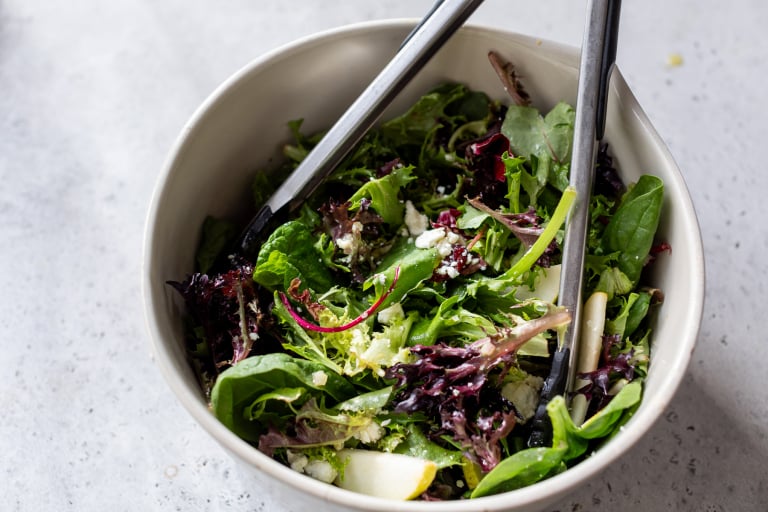 Using tongs to toss pear salad in bowl