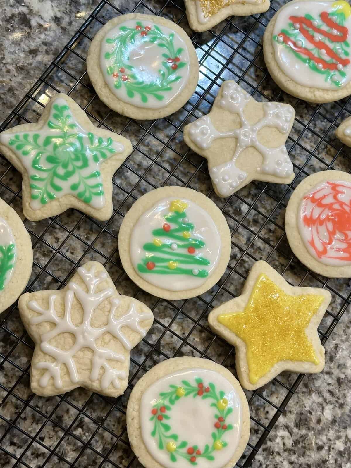 Christmas-themed sugar cookies with colorful icing designs on a cooling rack, including trees, wreaths, and stars.