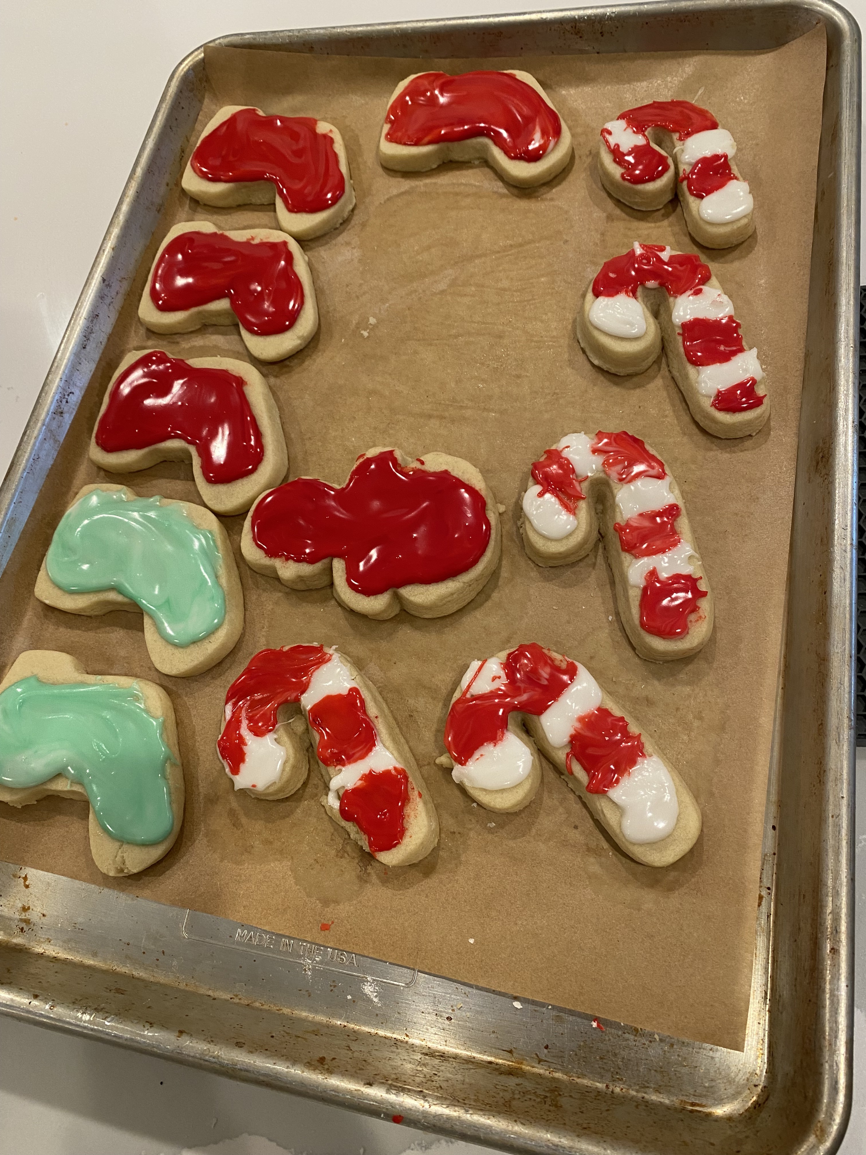 A baking tray with candy cane and stocking cookies decorated with red, white, and green icing.