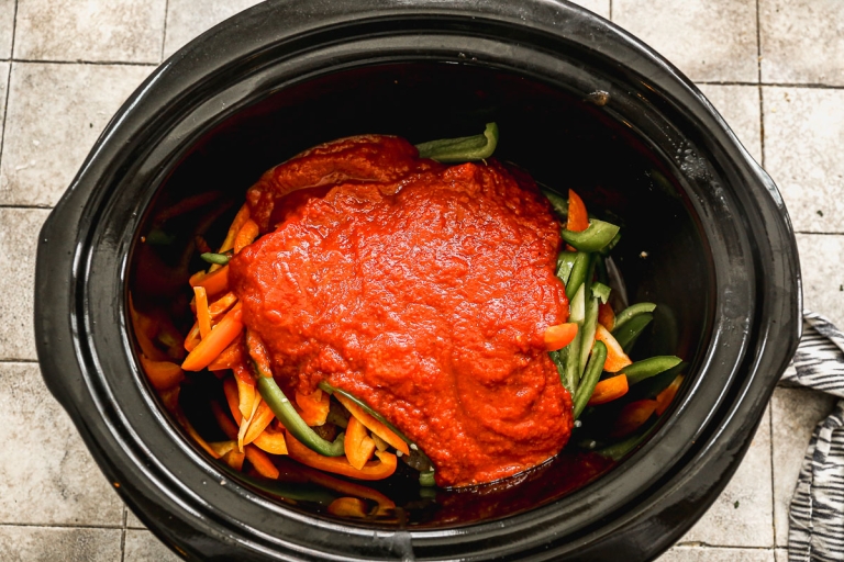 Sauce poured over peppers and sausage in crockpot