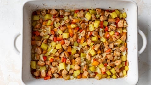 A rectangular baking dish filled with a roasted mix of diced potatoes, chunks of sausage, and pieces of bell peppers in various colors. Everything is seasoned and baked to a golden brown.